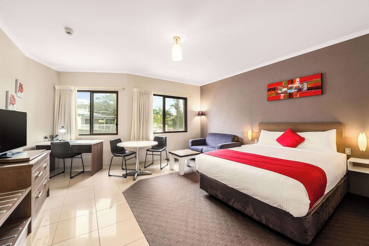 A hotel room with a bed, desk, chair, and a TV.