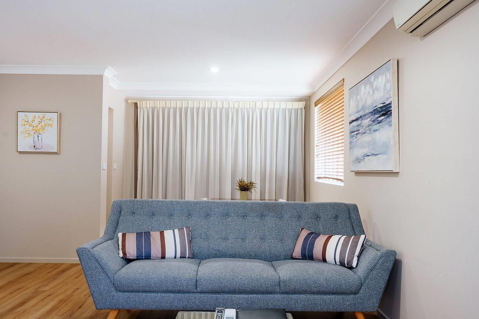 A living room with a grey sofa, two striped cushions, a vase with flowers, and a painting on the wall.