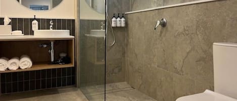 Et moderne badeværelse med en brusekabine i glas, et hvidt toilet, en vask med toiletartikler og en håndklæderække.