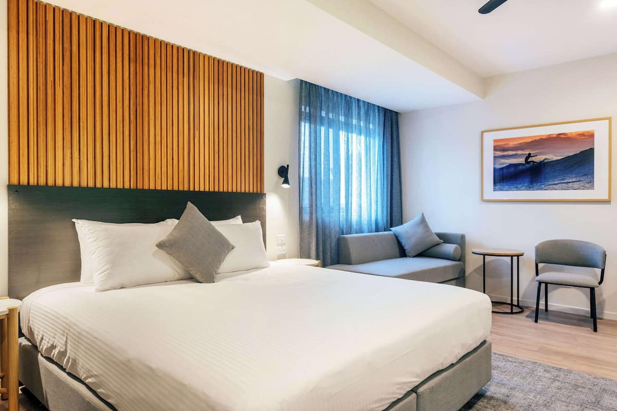A modern hotel room with a large bed, a sofa, a small table, and a chair.