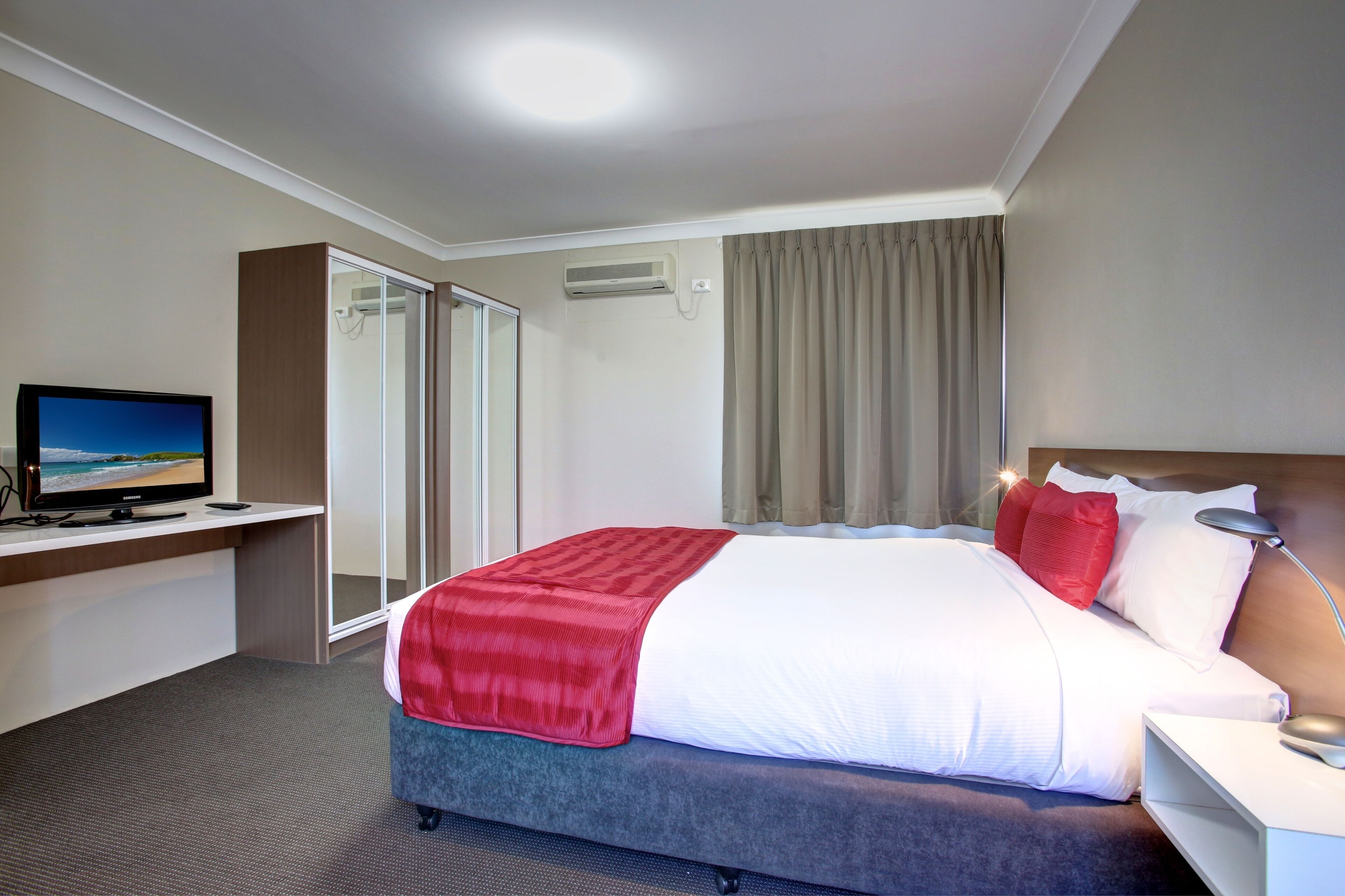 A hotel room with a bed, a desk with a computer, a TV, and a window with curtains.