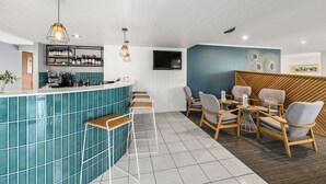 A modern bar area with a teal-tiled counter, bar stools, and a seating area with wooden chairs and tables. - Quality Hotel City Centre (Coffs Harbour)