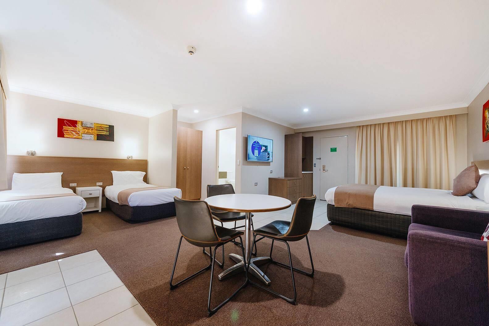 A hotel room with two beds, a dining table, and a TV.