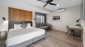 A modern hotel room with a large bed, a desk, a ceiling fan, and a view of the outdoors through the window. - Quality Hotel City Centre (Coffs Harbour)