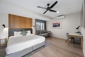 Una habitación de hotel moderna con una cama grande, un escritorio, un ventilador de techo y vistas al exterior por la ventana.