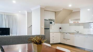 A modern kitchen with white cabinets, a microwave, and a sink. There is a dining table with a plant in the center.