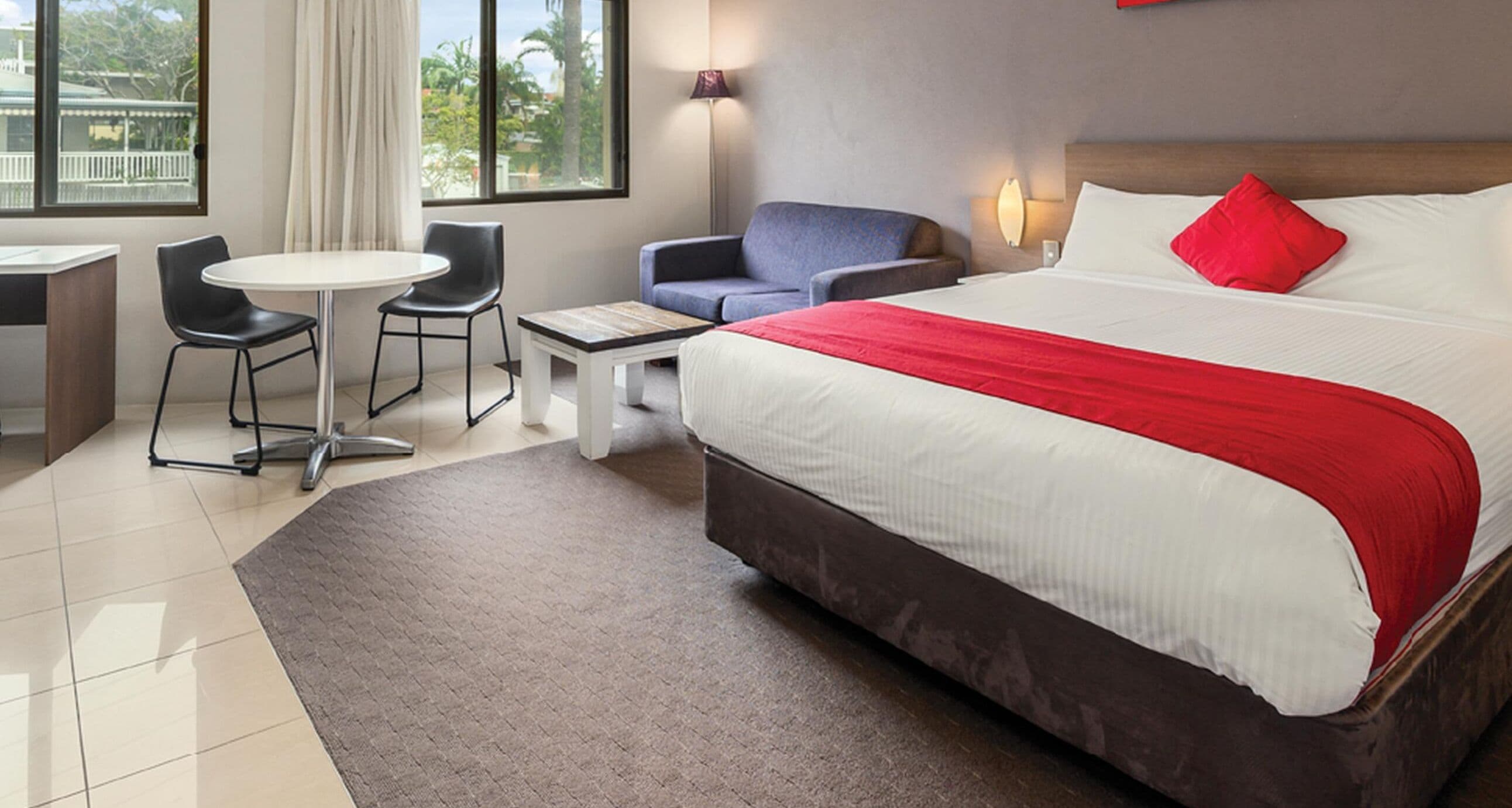 A hotel room with a large bed, a desk with a chair, a sofa, and a small table.