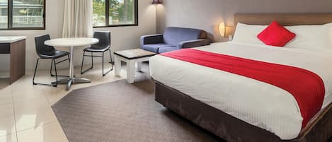 A hotel room with a large bed, a desk with a chair, a sofa, and a small table.