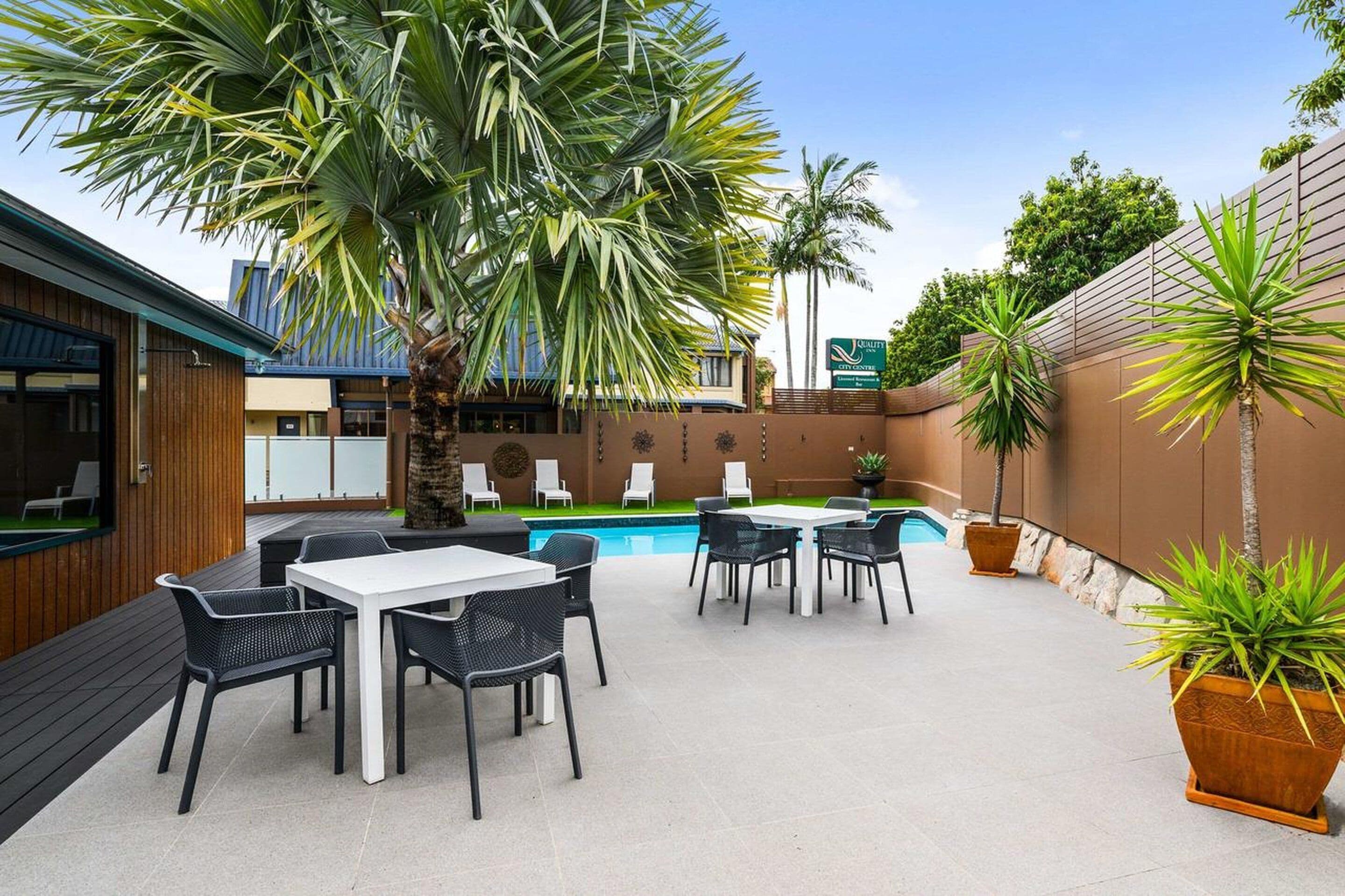 Un patio al aire libre con mesas y sillas, una piscina y palmeras.