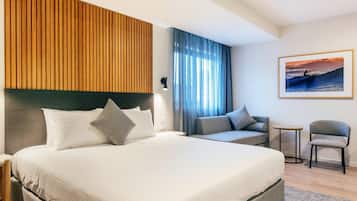 A hotel room with a large bed, a sofa, a small table, and a chair.