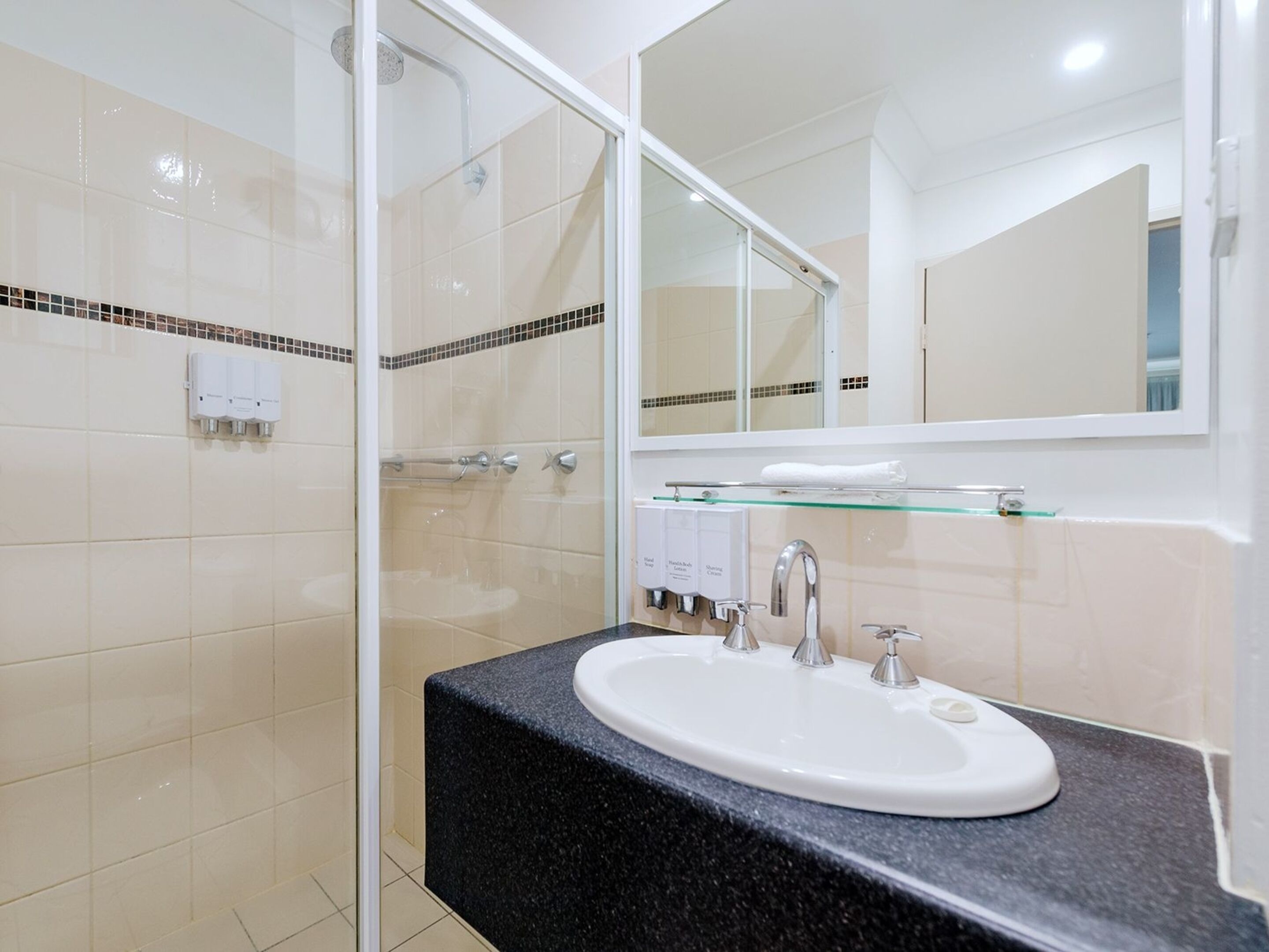 A modern bathroom with a glass shower enclosure, a white sink with a black countertop, and a large mirror above the sink.