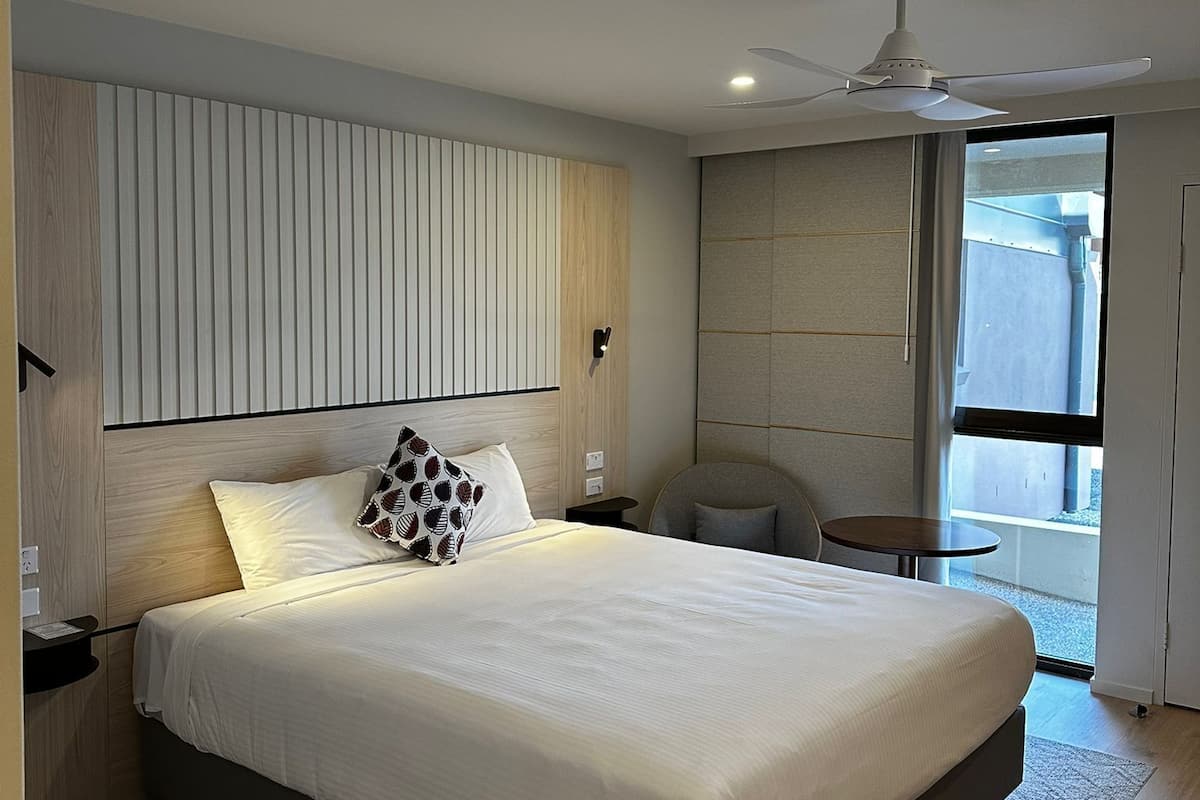 A modern hotel room with a large bed, a ceiling fan, a small table, and a view of the outside.
