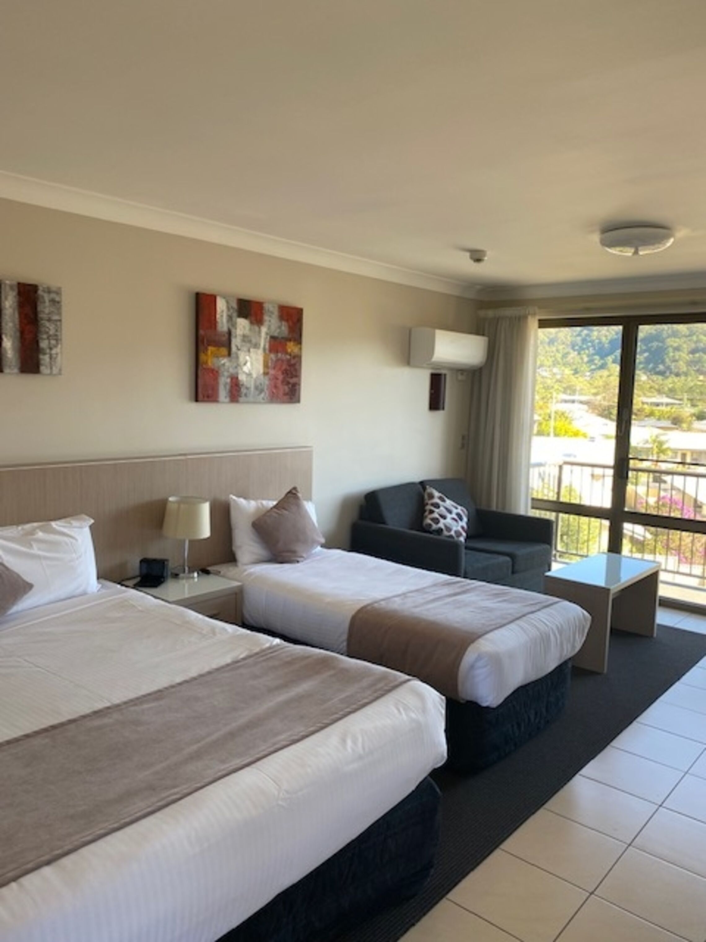 A hotel room with two beds, a sofa, a small table, and a balcony with a view.