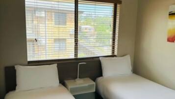 Quarto de hotel com duas camas de solteiro, um ventilador de teto e janela com persianas.