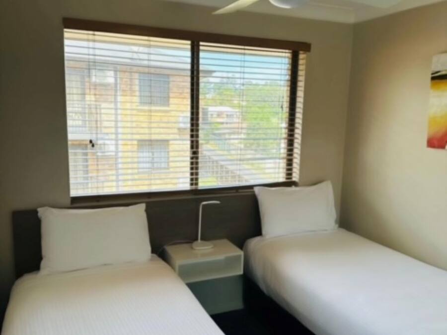 Quarto de hotel com duas camas de solteiro, um ventilador de teto e janela com persianas.