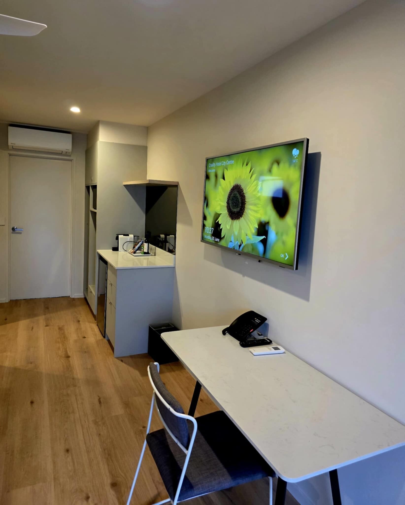 Una habitación de hotel moderna con un televisor grande montado en la pared, un escritorio con un teléfono y una silla.