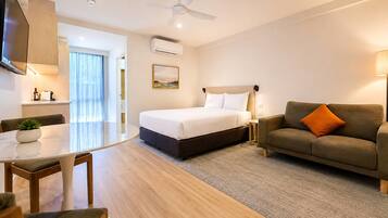 A modern hotel room with a bed, a sofa, a dining area, and a ceiling fan.