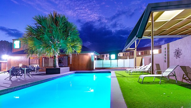 A swimming pool with lounge chairs, a palm tree, and a covered area with a view of the pool. - Quality Hotel City Centre (Coffs Harbour)