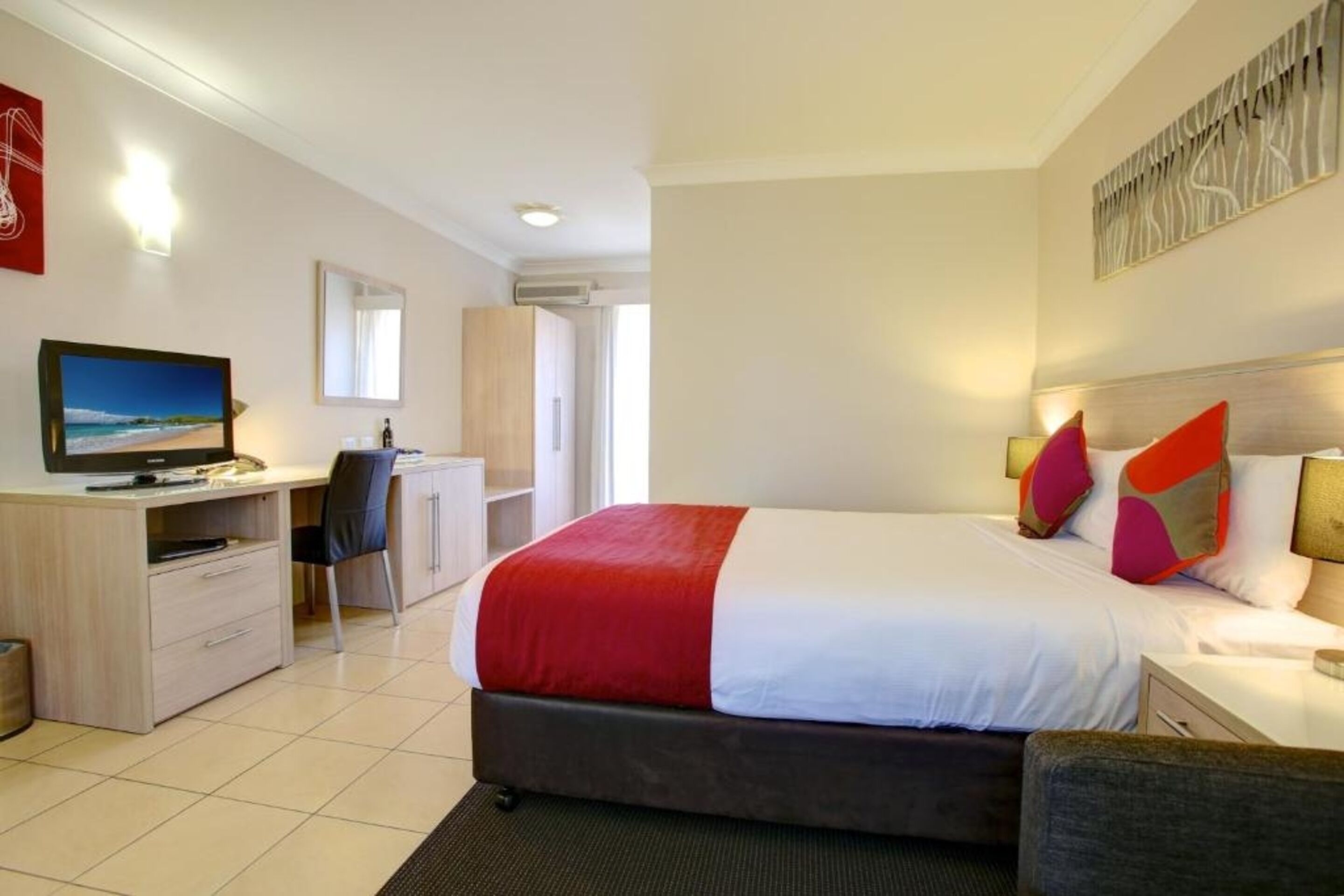 A hotel room with a bed, a desk, a chair, a TV, and a window.