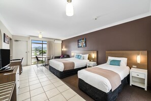 Habitación de hotel con dos camas, un escritorio con computadora, una silla y vista al exterior.