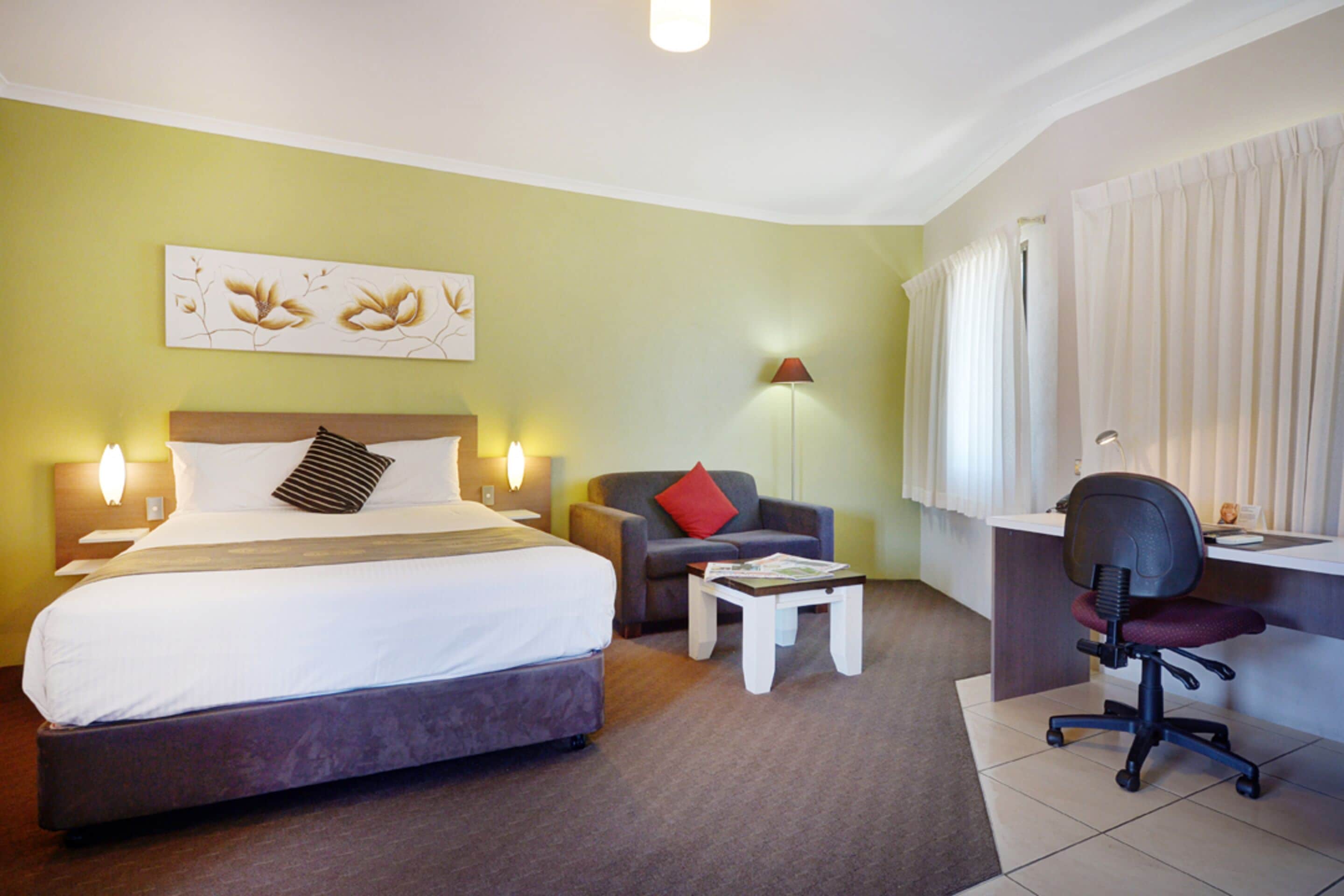 Una habitación de hotel con cama, escritorio, silla, lámpara y un cuadro en la pared.