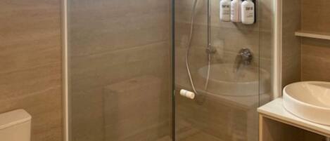 A bathroom with a glass-enclosed shower, a white sink, and toiletries on a shelf.