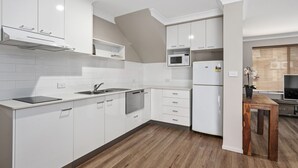 A modern kitchen with white cabinetry, a built-in microwave, and a wooden dining table. - Quality Hotel City Centre (Coffs Harbour)