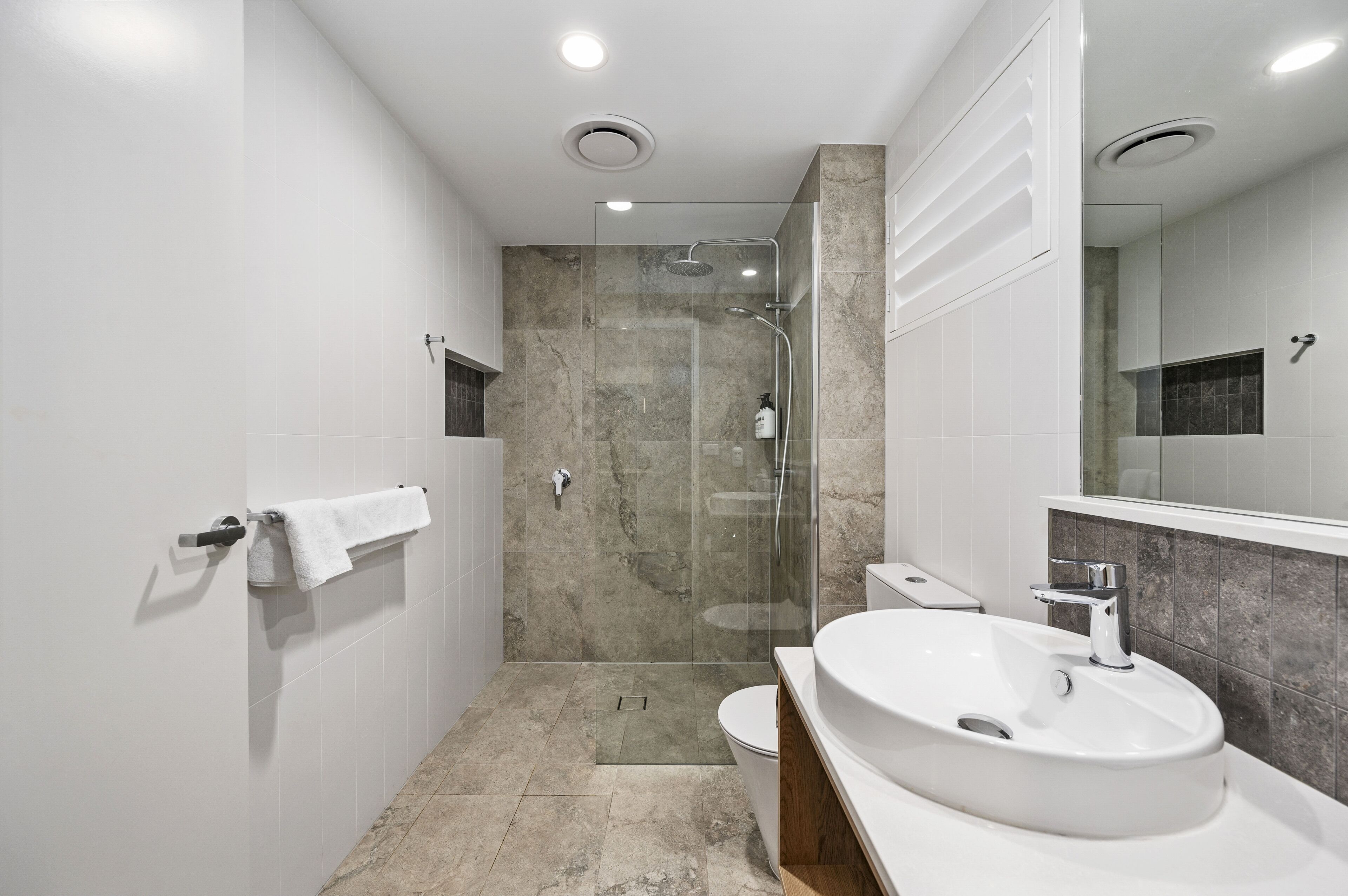 A modern bathroom with a glass-enclosed shower, a white sink, and a large mirror.