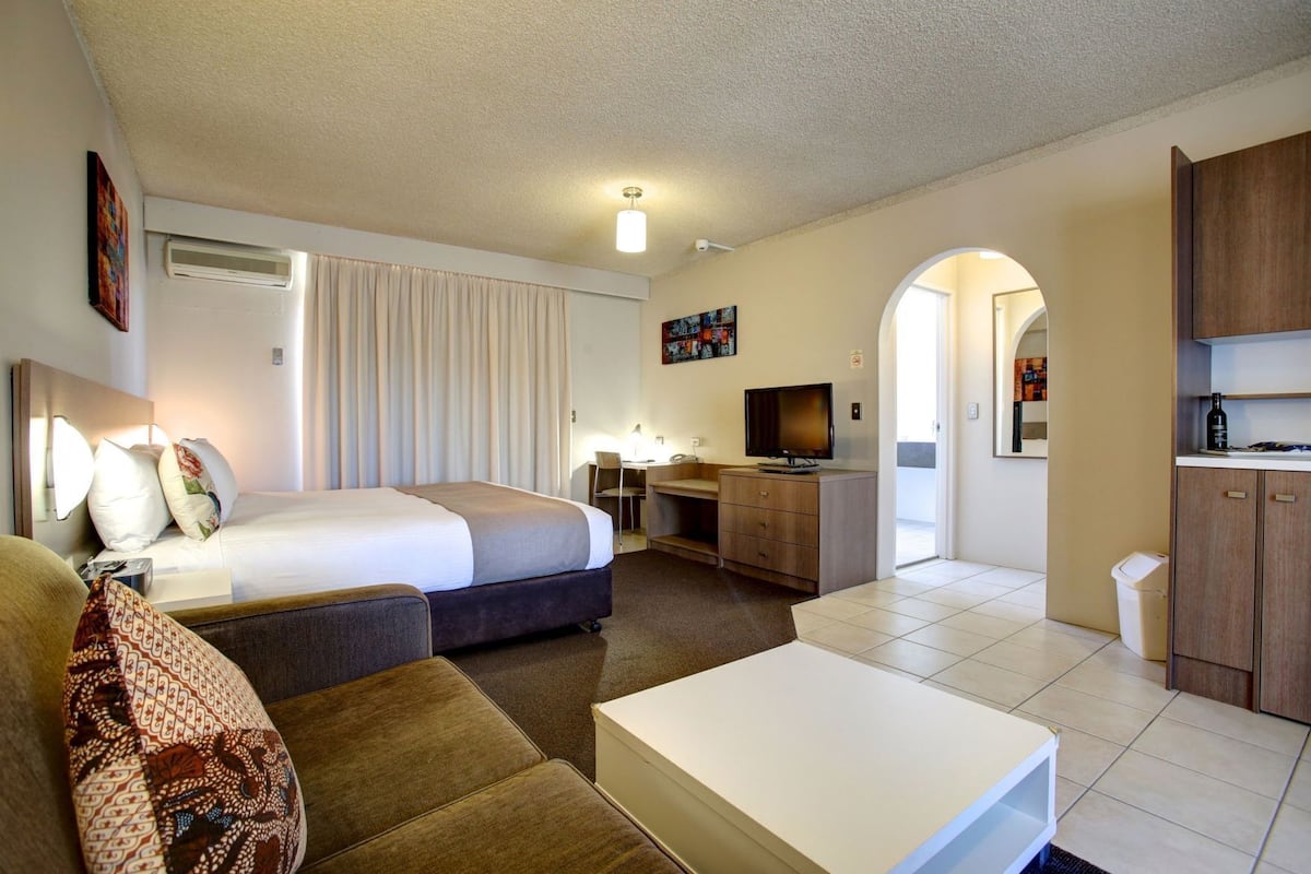 A hotel room with a bed, a desk, a television, a sofa, and a kitchenette.