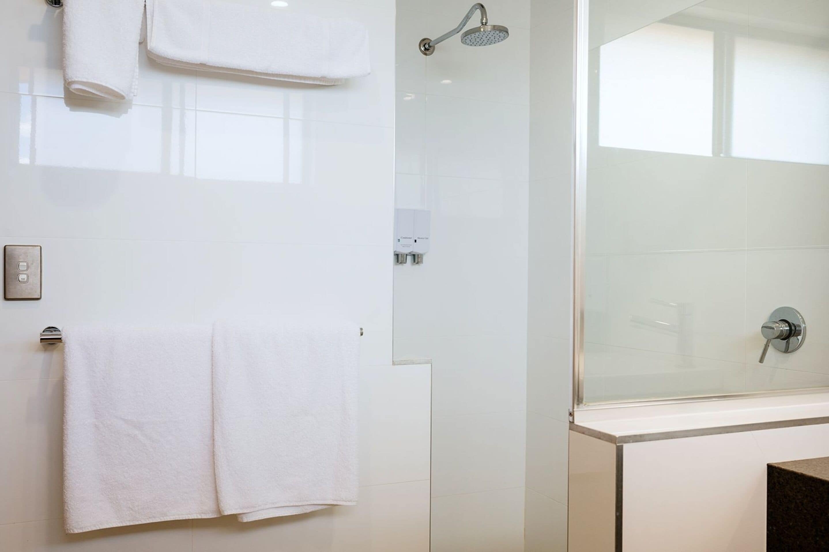 Un bagno moderno con cabina doccia in vetro, un asciugamano bianco appeso al muro e un pannello di controllo ben visibile.