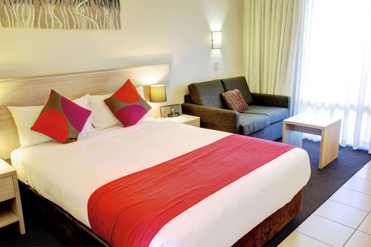 A hotel room with a large bed, a sofa, a nightstand, and a small table.