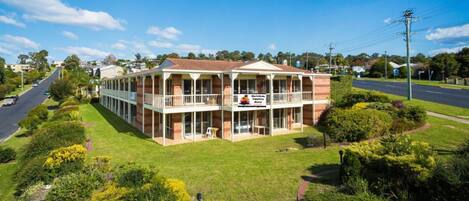 A two-story motel with a balcony on the ground floor, surrounded by well-maintained lawns and a clear blue sky.