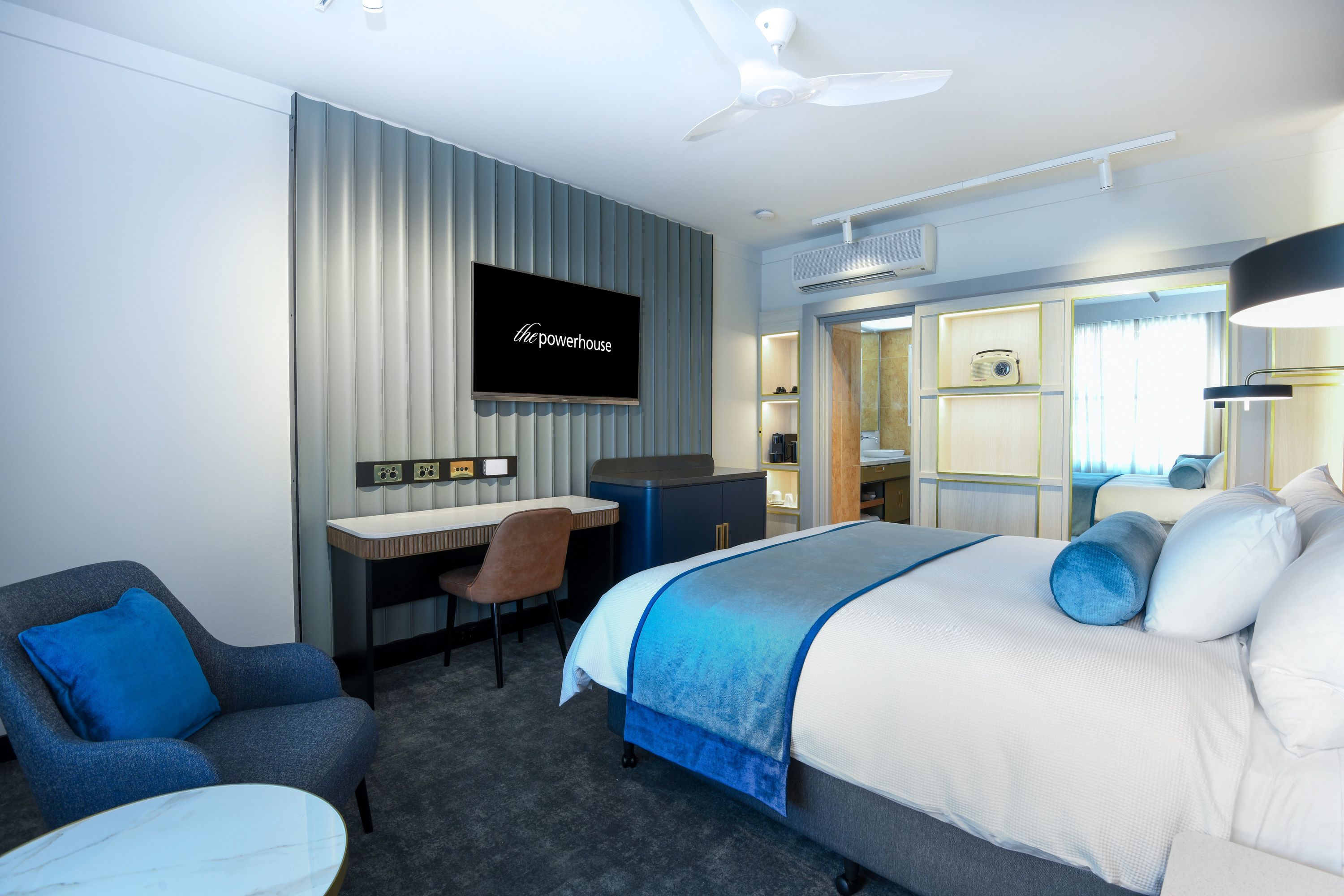 A modern hotel room with a bed, a desk, a chair, a television, and a wardrobe.