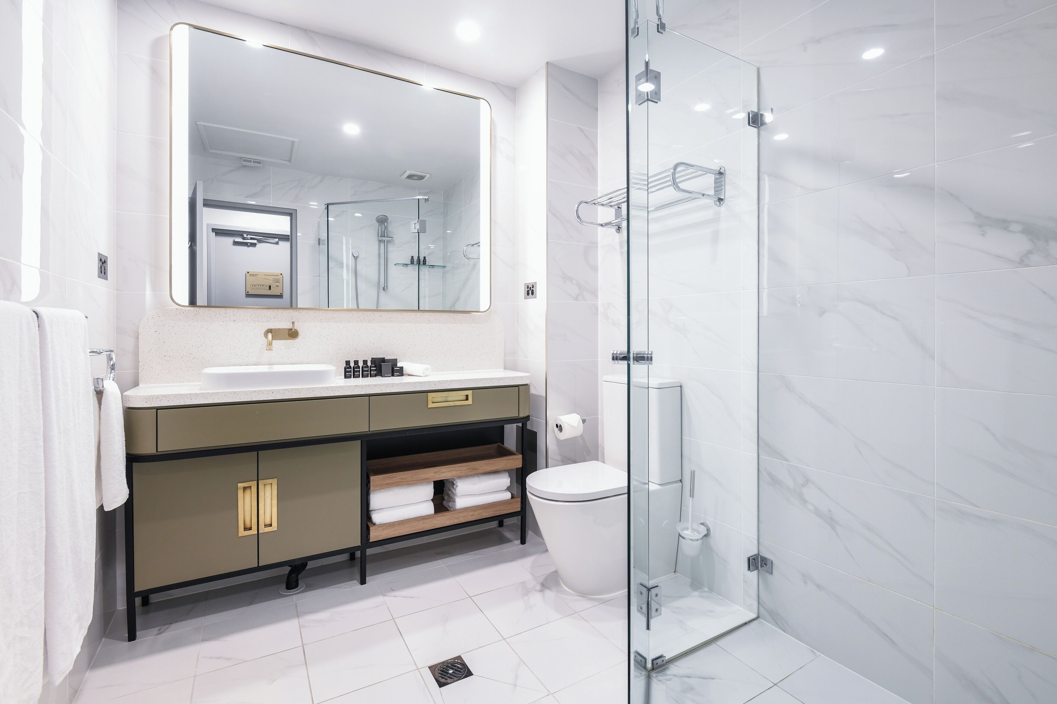 Une salle de bain moderne avec un grand miroir, un lavabo, des toilettes et une douche à parois de verre.