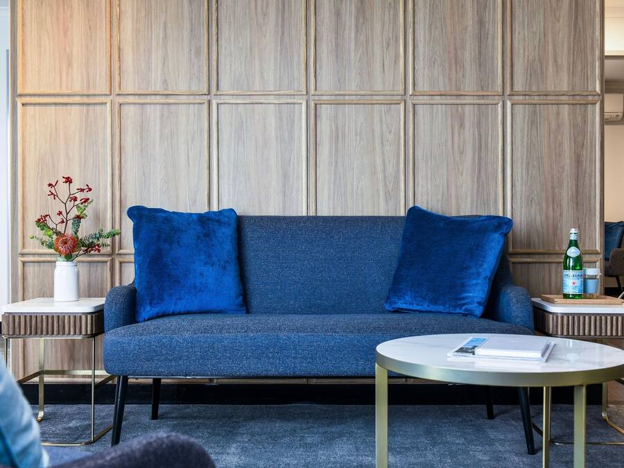 Un salon moderne avec un canapé bleu, deux coussins assortis, une petite table d’appoint blanche, une table basse ronde et un vase décoratif avec des fleurs.