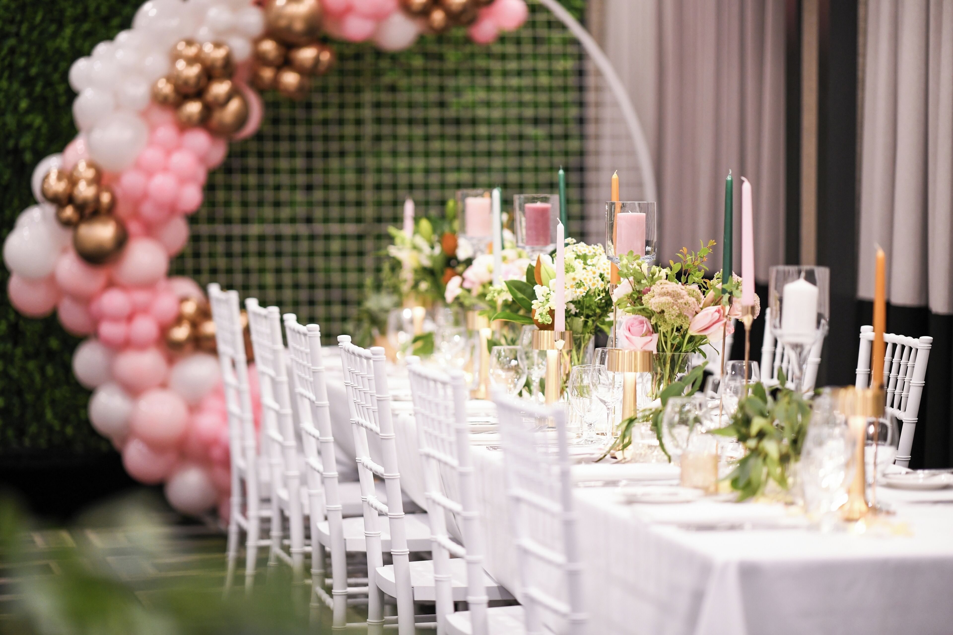 A table set with white chairs, pink and gold balloons, and candles.