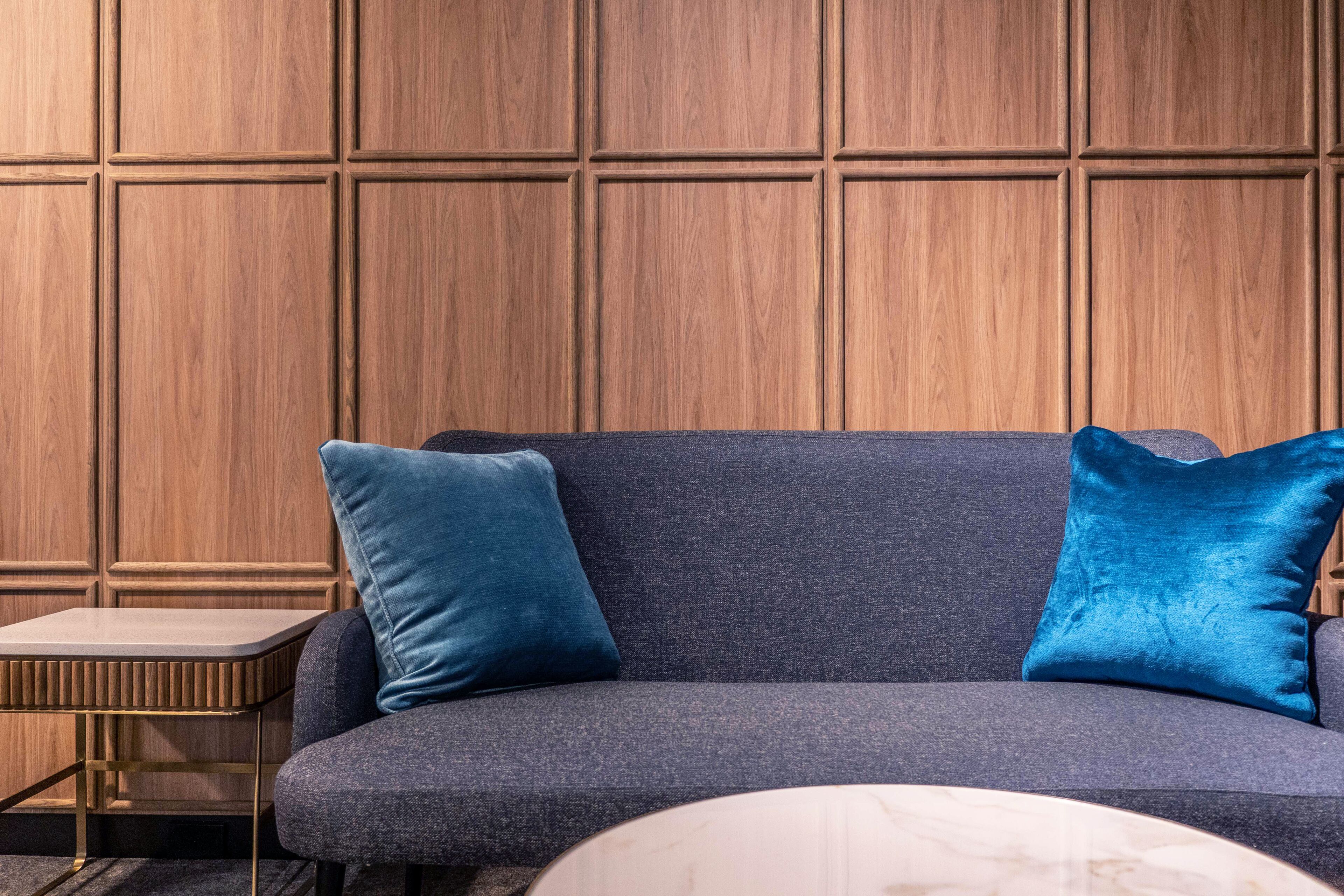 Ein modernes Wohnzimmer mit einem dunkelblauen Sofa, zwei passenden Kissen, einem kleinen Beistelltisch und einem Marmor-Couchtisch.