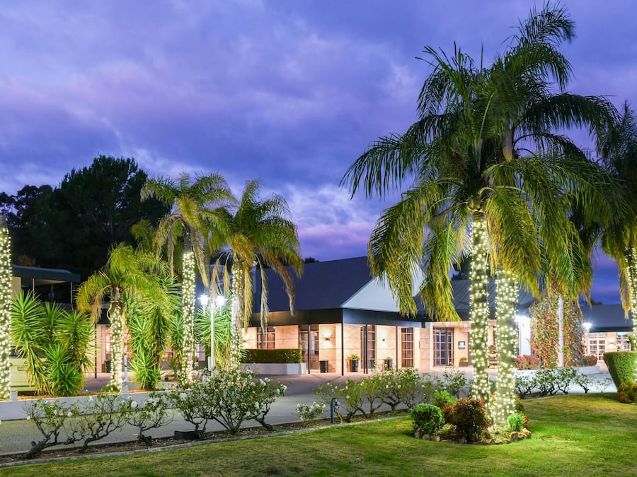 A hotel with a modern design, featuring a well-maintained garden with palm trees and other greenery.