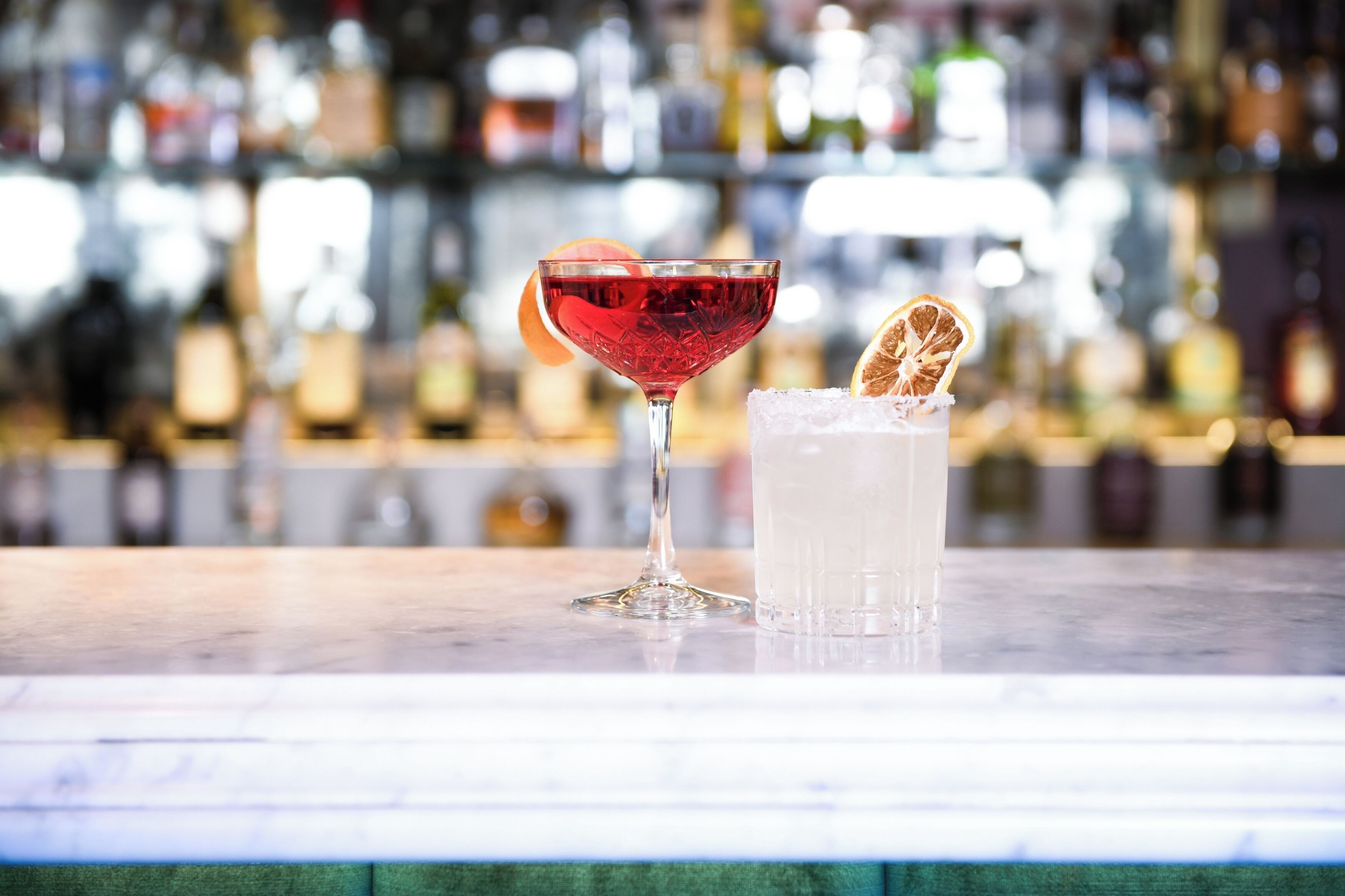 A bar setting with a cocktail glass and a clear drink on a marble surface.