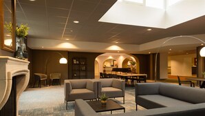 A modern lobby with sofas, a fireplace, and a dining area. - NH Eindhoven Conference Centre Koningshof (Veldhoven)
