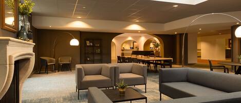 A modern lobby with sofas, a fireplace, and a dining area.