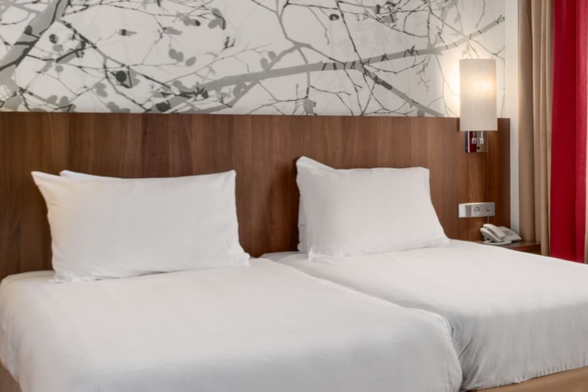 A hotel room with two beds, a wooden headboard, a wall-mounted lamp, and a telephone on the nightstand.