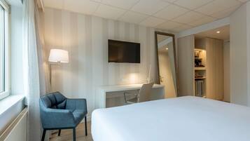 Habitación de hotel con cama, escritorio, silla, televisión y espejo.