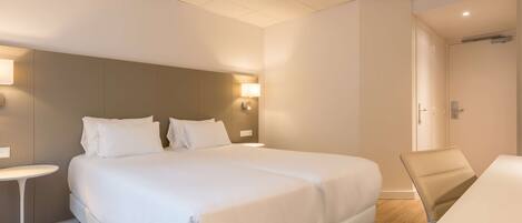 A modern hotel room with a large bed, a small round table, and a desk with a chair.