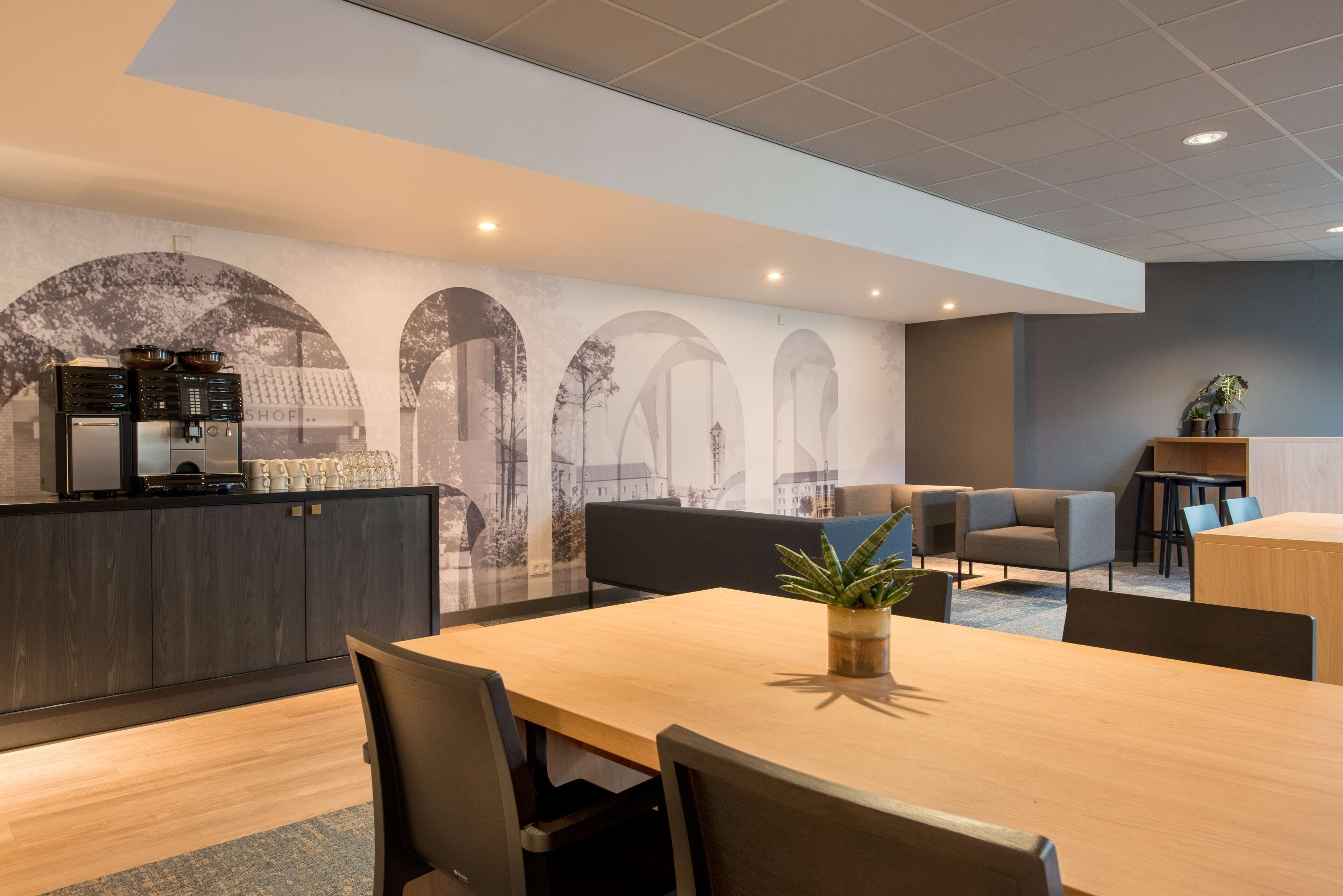 A modern hotel lobby with a wooden reception desk, seating area, and a mural on the wall.