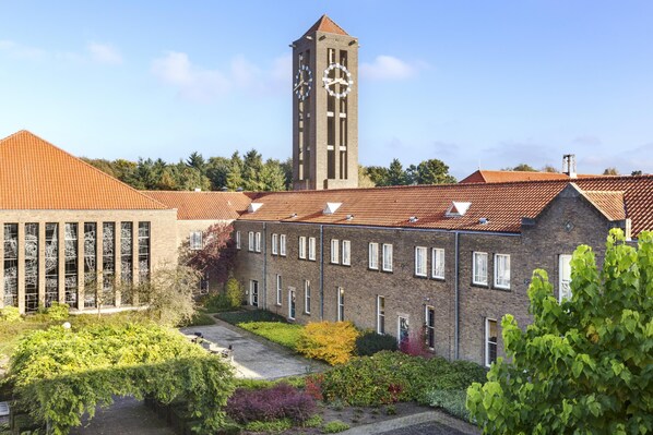 Ein Gebäude mit einem Glockenturm, einer Ziegel-Fassade und einem Garten.