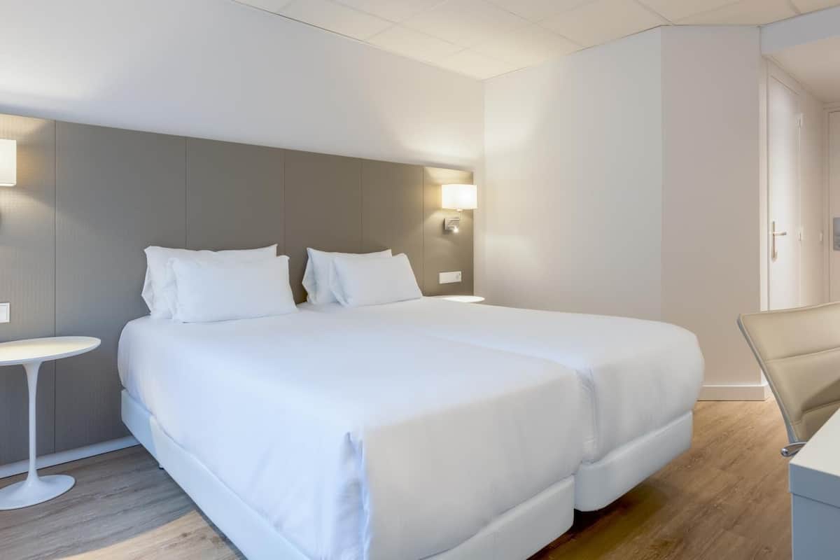 A modern hotel room with a large bed, a bedside table, a chair, and a desk.