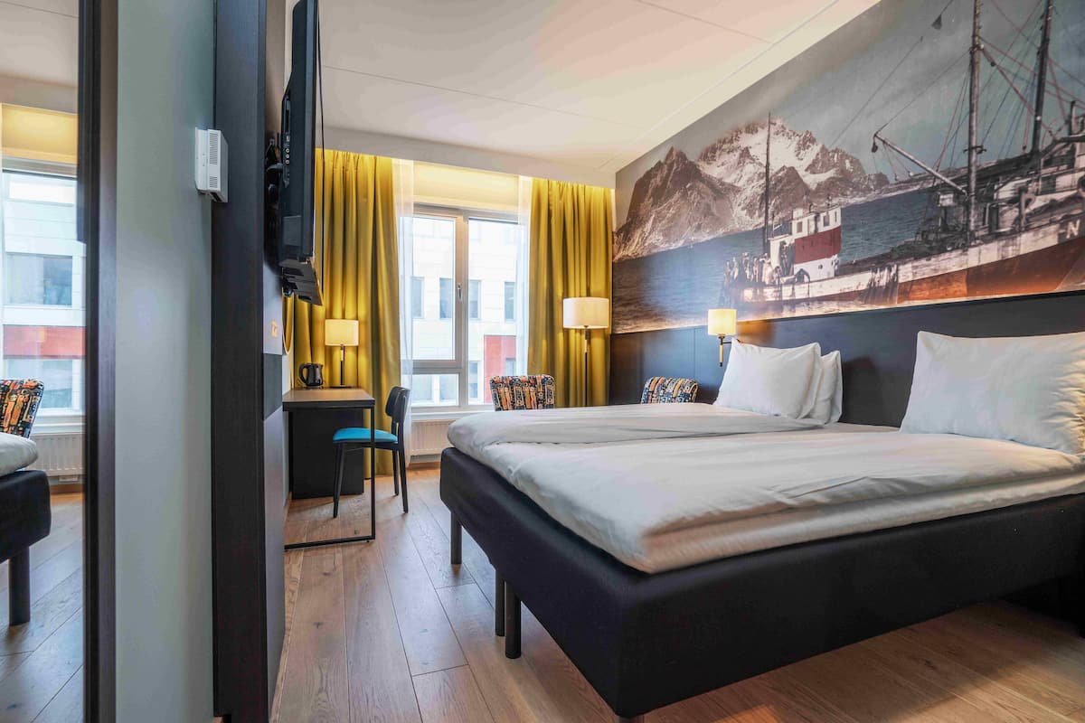 A hotel room with a large bed, a desk with a chair, a television, and a painting of a boat on the wall.