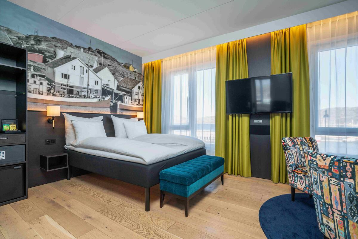 A modern hotel room with a large bed, a bench, a TV, and a mural on the wall.