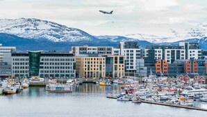 A marina with boats, a modern building complex, and snow-capped mountains in the background. - Thon Hotel Nordlys (Bodo)